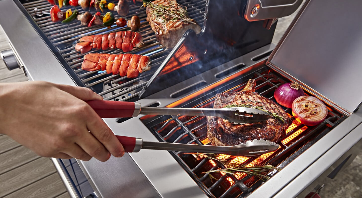 Person grilling steak and vegetables on an outdoor grill