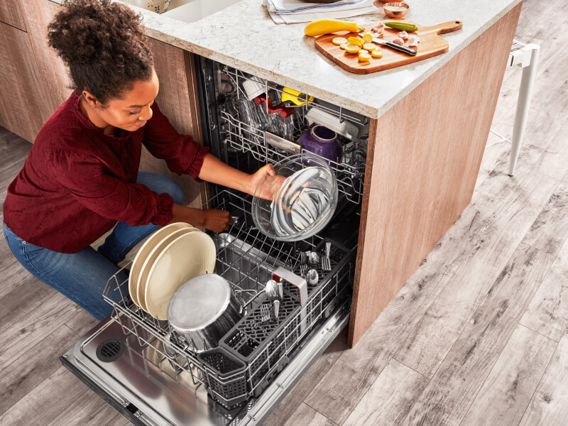 Person loading a glass mixing bowl into the bottom rack of a dishwasher