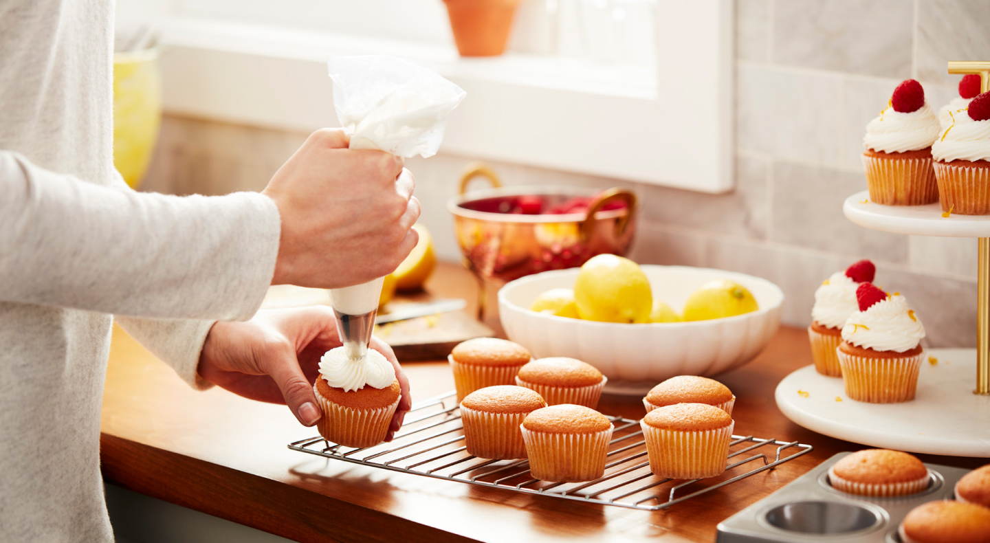 Person decorating cupcakes with vanilla buttercream frosting