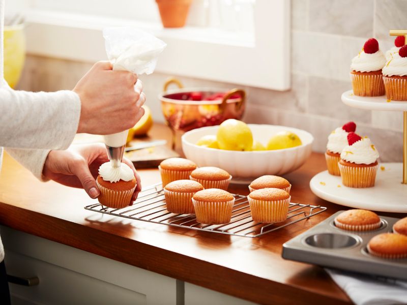 Person decorating cupcakes with vanilla buttercream frosting