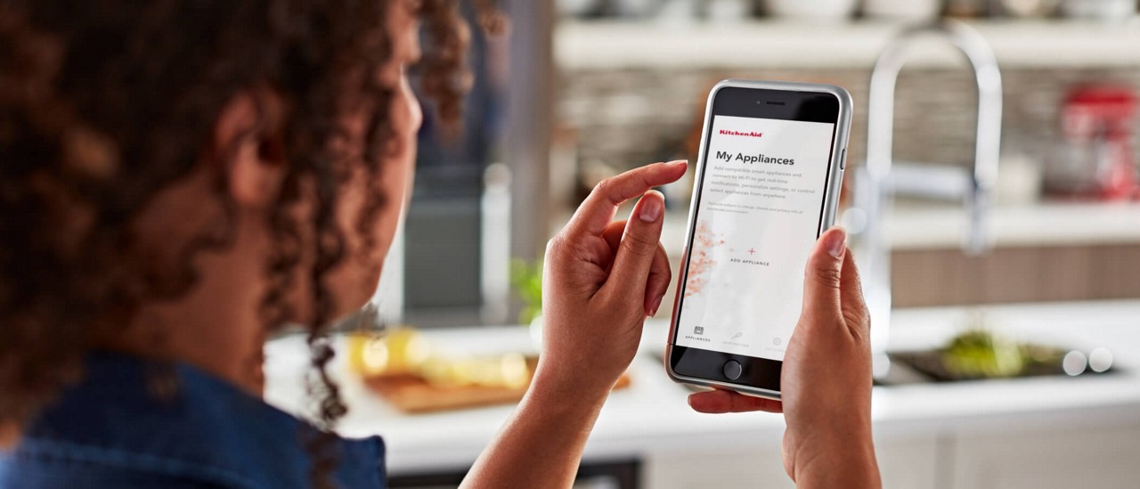 A woman using the KitchenAid™ app on her smartphone to add her connected appliances.