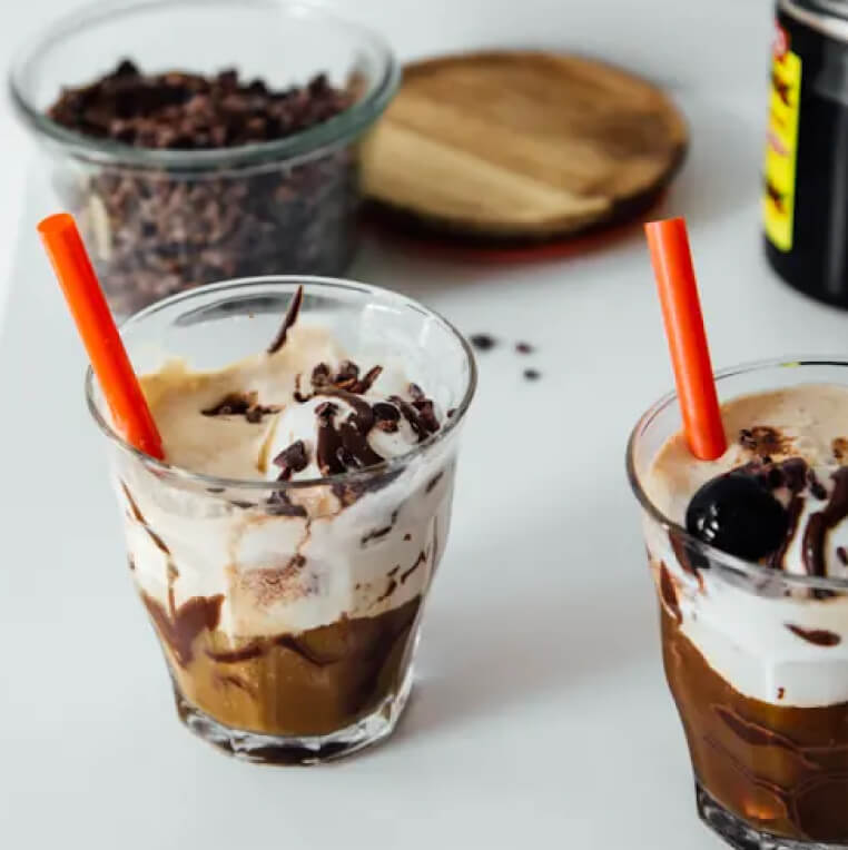 Two cups of cold brew coffee floats with a glass container of coffee beans in the background.