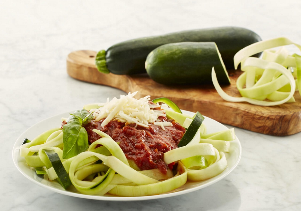 Zucchini noodles in white bowl with red sauce and grated parmesan