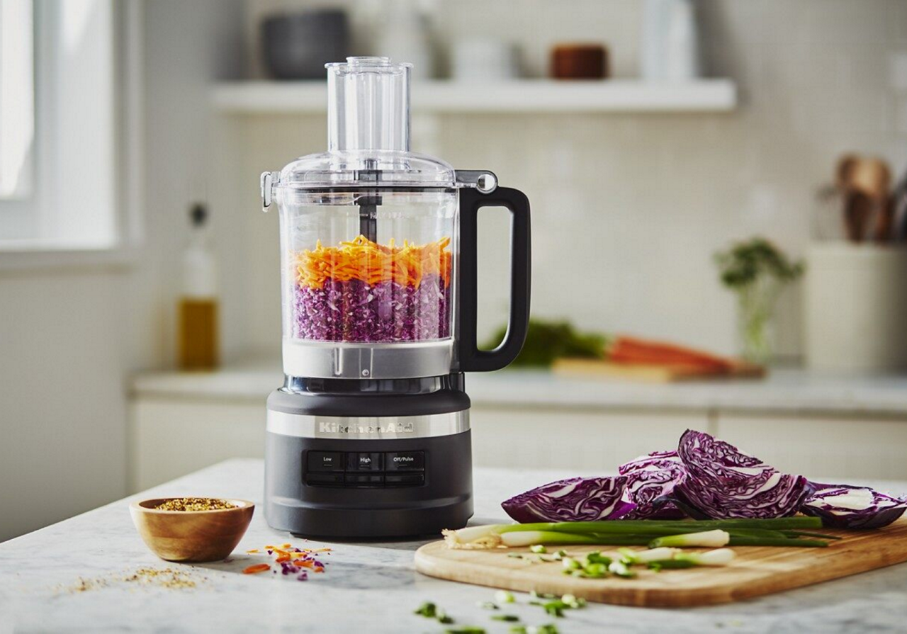 Black food processor filled with shredded carrots and purple cabbage
