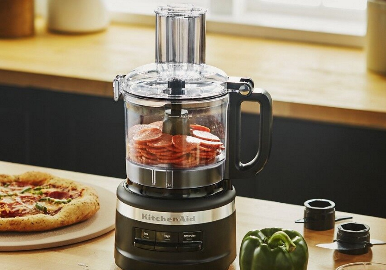 Black food processor filled with pepperonis on kitchen counter