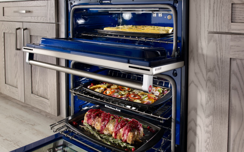 An open oven with a roast on the bottom rack and vegetables on the top rack
