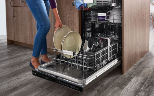 Person loading plates into the bottom rack of a built-in dishwasher