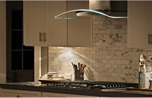 A glass canopy hood with LED lights illuminating a gas cooktop underneath
