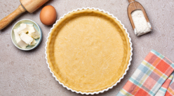 A tart crust and various baking implements and ingredients on a grey countertop.